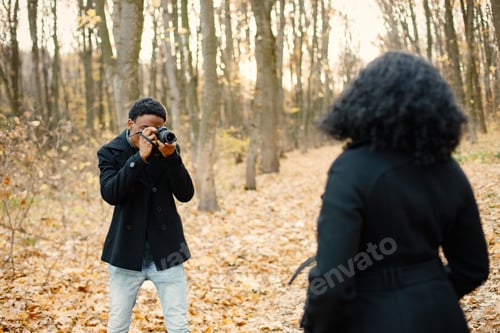 Preview: Black man take a photo of black woman in autumn park