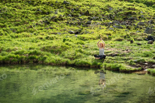 Preview: Attractive young woman enjoying nature and practice yoga in front of a mountain lake.