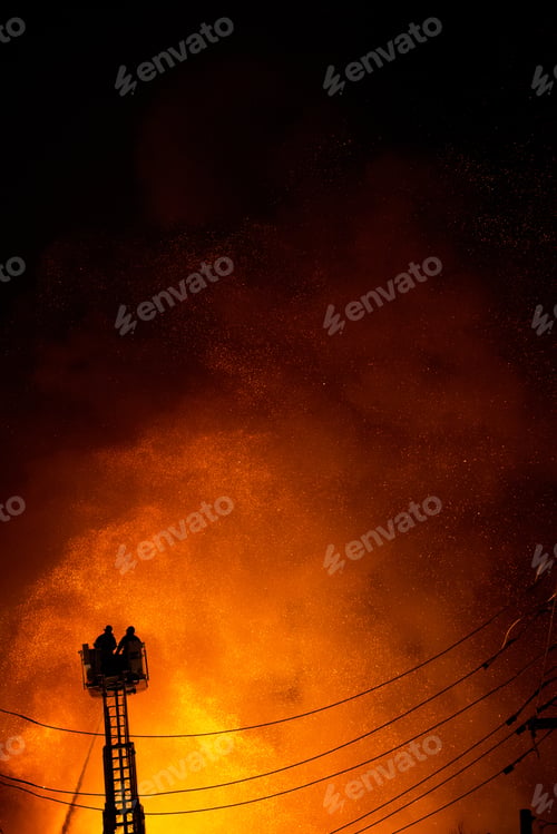 Preview: Fire fighters on top of ladder fighting building on fire at night