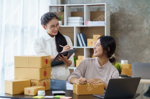 Preview: Two beautiful Asian female online business owner preparing parcels for delivery to customers.