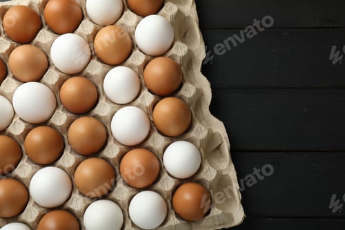 Preview: Many raw chicken eggs in carton on black wooden table, top view. Space for text