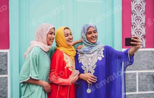 Preview: Happy Muslim girls taking selfie with mobile smartphone camera outdoor