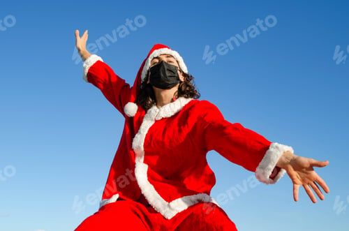 Preview: Young caucasian male wearing a Santa Claus costume and medical mask - the concept of new normal