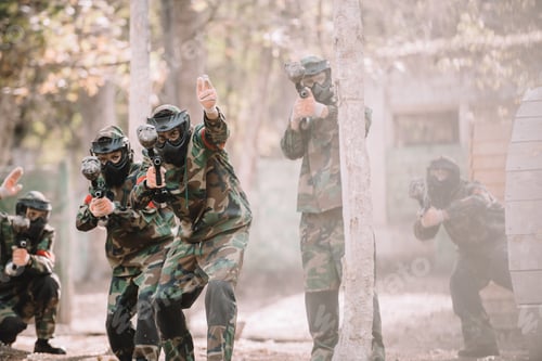 Preview: paintball player in camouflage uniform pointing by hand to his team with markers guns outdoors