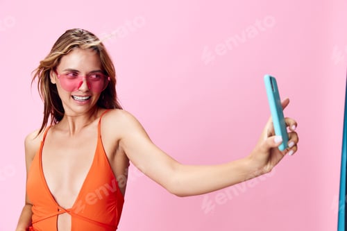 Preview: Capturing the perfect moment a woman in a vibrant orange swimsuit snapping a selfie against a pretty