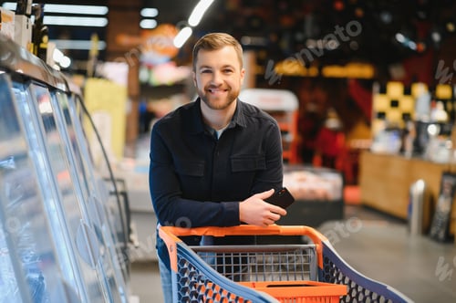 Preview: Young man buying groceries at the supermarket. Other customers in background. Consumerism concept.