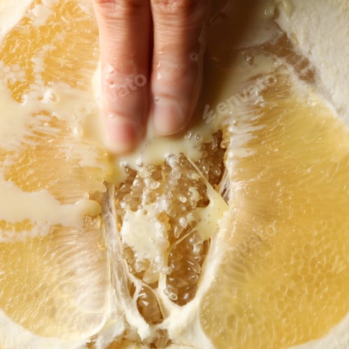 Preview: Female fingers with condensed milk on ripe pomelo fruit, close up