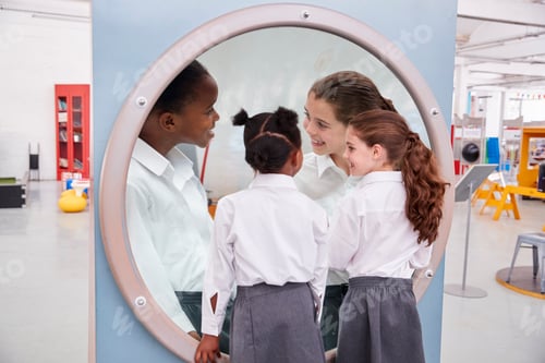 Schoolgirls looking in a magnifying mirror at science centre