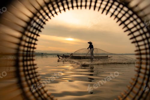 Preview: Silhouette of fisherman at sunrise, Standing aboard a rowing boat and casting a net