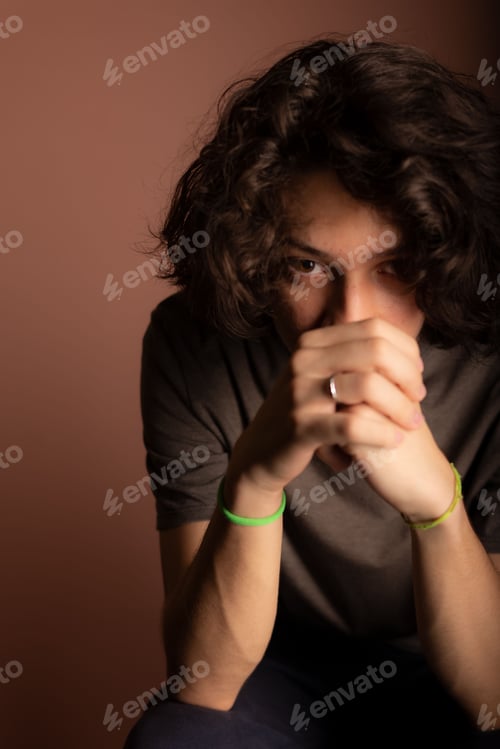Preview: Caucasian male with curly hair sitting in front of a wall in a thoughtful pose