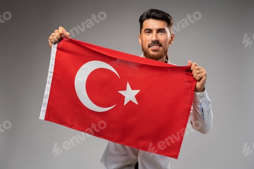 Preview: Young businessman holding a flag of Turkey on gray background