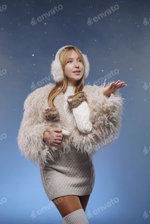 Preview: Full length winter fashion model in knit dress and earmuffs with falling snow