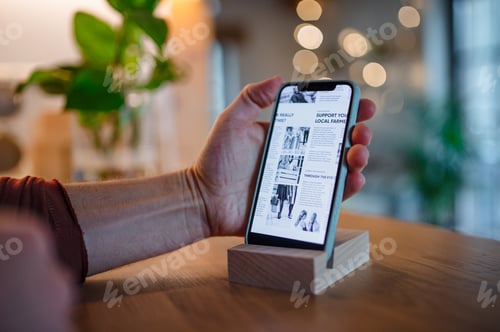 Preview: Smartphone in wooden stand holder on table indoors at home or on office.