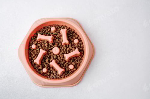 Preview: Pink dog bowl filled with kibble and bone shaped treats on a textured white surface.