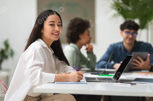 Preview: Asian Businesswoman Near Laptop Sitting At Desk With Coworkers Indoors