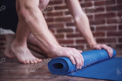 Preview: Athletic Man Rolling Up Yoga Mat on Floor