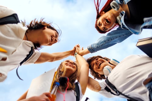 Preview: Happy students joining hands celebrating success outdoors