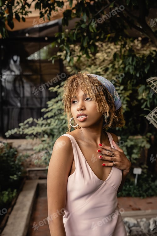 Preview: Portrait of stylish young african american woman in headscarf and summer dress touching chest