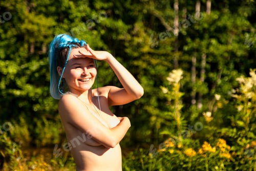 Preview: Portrait of naked woman nudist with bare slim body covering breast on nature, laughing