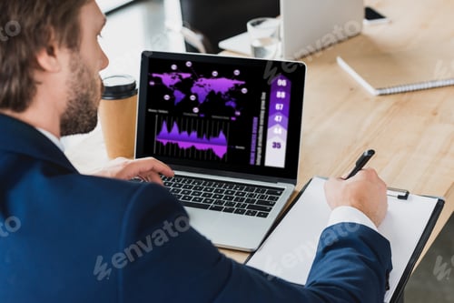 Preview: cropped shot of businessman taking notes on clipboard and using laptop with business graphs on