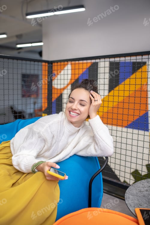 Preview: Young woman sitting on bag chair, holding mobile phone