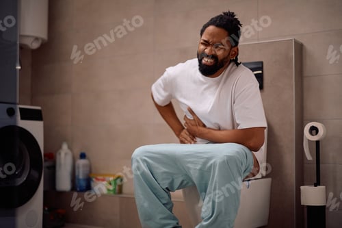 Preview: Black man with stomachache sitting on a toilet.