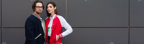 Preview: young couple in stylish jackets looking at camera near grey wall, banner