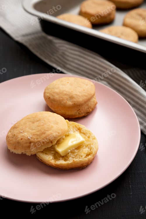 Preview: Homemade Flaky Buttermilk Biscuits on a pink plate on a black background, side view.