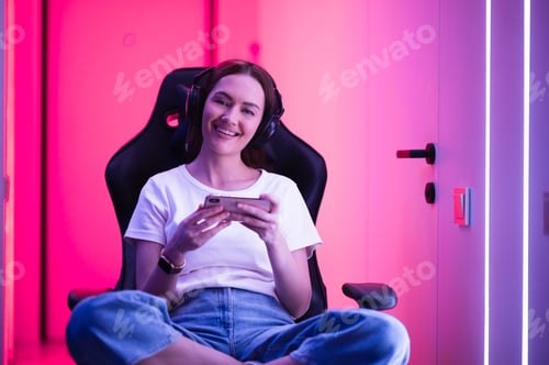 Preview: Gamer girl in a big professional music headset holds smart phone and plays game app