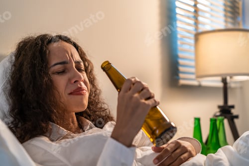 Preview: Drunk Latino woman hold beer bottle, and crying feel hangover on bed.