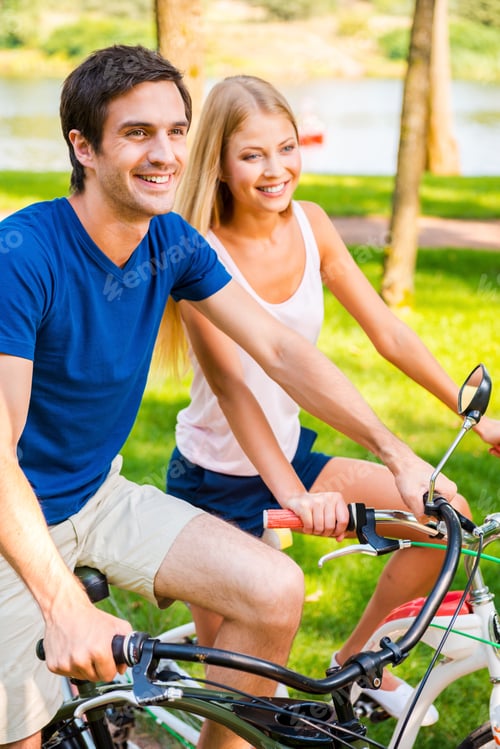 Preview: Riding bicycle is fun! Beautiful young smiling couple riding their bicycles in park together