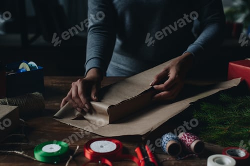 Preview: cropped shot of woman wrapping book in kraft paper as christmas gift