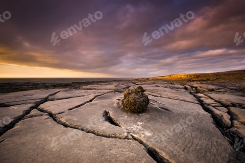 Preview: A lonely boulder rests on cracked earth under a dramatic sunset sky.