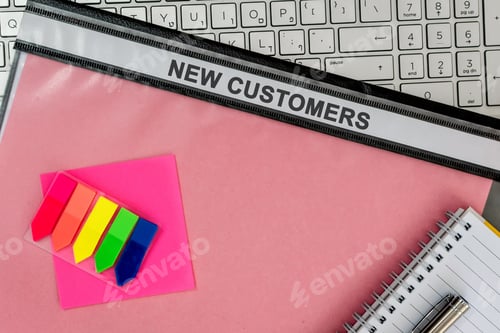Preview: Notepad with a pencil on a pink folder labelled "NEW CUSTOMERS" on a laptop in the office