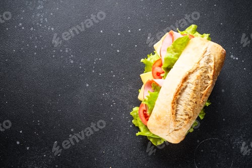 Preview: Ciabatta sandwich with lettuce, cheese, tomatoes and ham on black table.