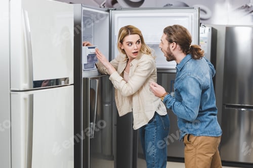 Preview: shocked boyfriend and girlfriend standing near fridge in home appliance store