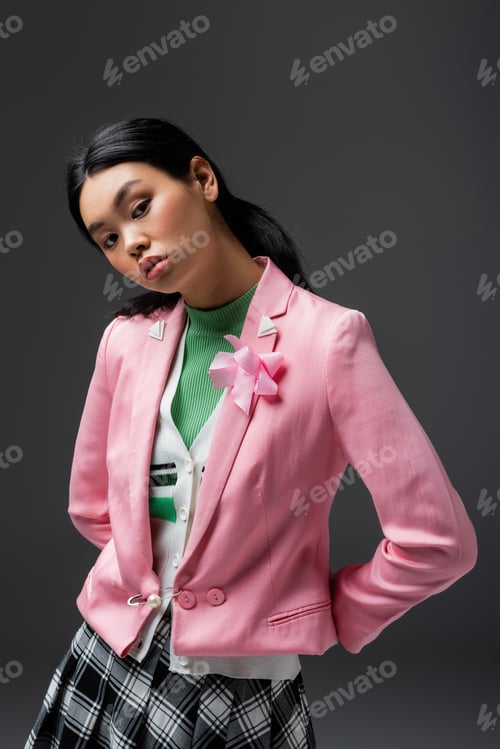 Preview: Trendy young asian model in pink jacket looking at camera isolated on grey