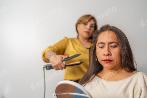 Preview: Hairdresser straightening hair of a customer looking in the mirror