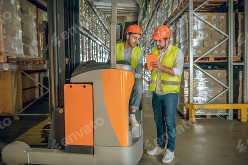 Preview: Talking Business. Two Warehouse Workers In Helmets Having A Lively Conversation