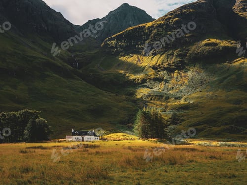 Preview: House in a field with a black roof surrounded by high and beautiful mountains in Glencoe, Scotland