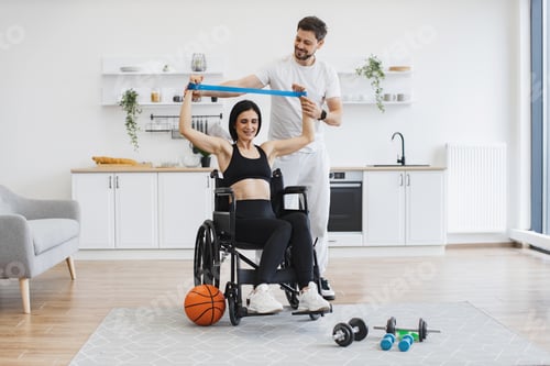 Preview: Husband helping mature woman in wheelchair lifting arms with stretching bands.