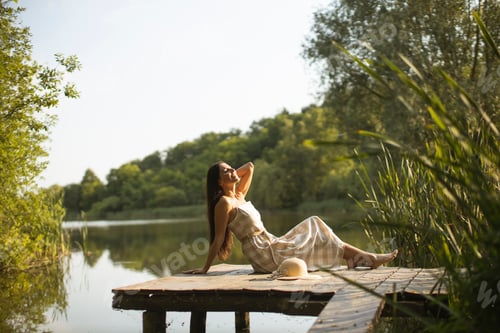 Preview: Relaxing young woman on wooden pier at the lake