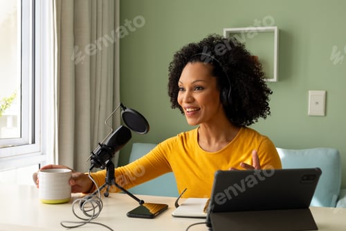 Vista previa: Happy biracial woman using headphones, tablet and microphone podcasting from home
