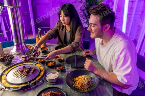 Preview: a couple in love having dinner in a Korean restaurant picking up juicy meat from grill with tongs
