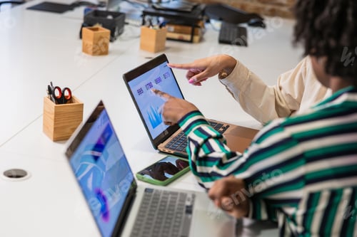 Preview: Businesswomen analyzing data charts on convertible laptop in modern office