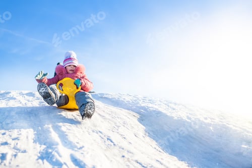 Preview: Happy small girl in winter clothing riding downhill