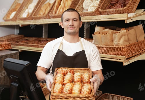 Preview: Portrait of professional baker holding tray with fresh buns near showcase in store