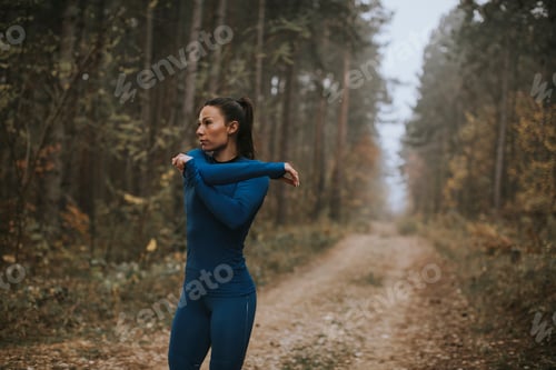 Preview: Young woman in blue track suit stretching before workout in the autumn forest