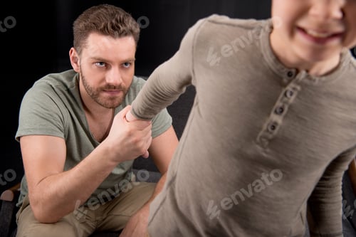 Preview: Cropped shot of angry father holding hand of scared little son, family problems concept