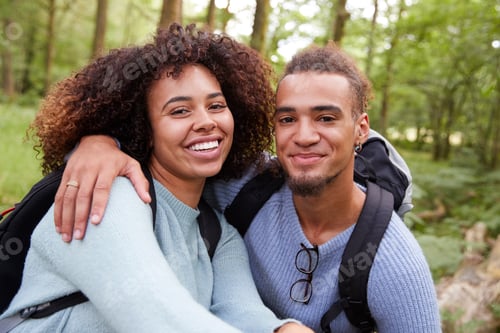 Vista previa: Una joven pareja mestiza sonriendo a la cámara durante una caminata en un bosque, retrato de cerca